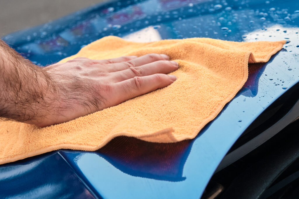 Cleaning or polishing of a blue car with microfiber cloth. Manual car washing service